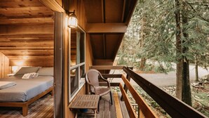 Una cabaña de madera con balcón, cama, silla y mesa.