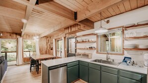 Una cocina moderna con vigas de madera, armarios verdes y una isla central con lavavajillas.