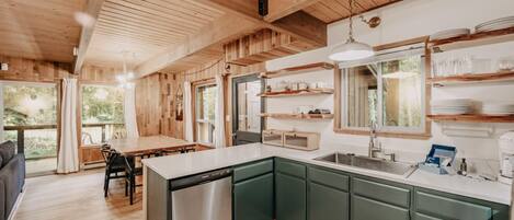 A modern kitchen with wooden beams, green cabinets, and a central island with a dishwasher.