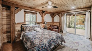 A wooden cabin bedroom with a bed, a chair, a nightstand, and a window. - Glacier Springs Cabin #39 - New Modern-rustic Cabin With Air Conditioning! (Deming)
