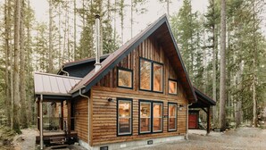 A wooden cabin with a sloped roof, large windows, and a chimney. - Glacier Springs Cabin #39 - New Modern-rustic Cabin With Air Conditioning! (Deming)