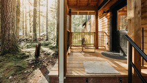 A wooden cabin with a porch, a fireplace, and a view of the forest. - Glacier Springs Cabin #39 - New Modern-rustic Cabin With Air Conditioning! (Deming)
