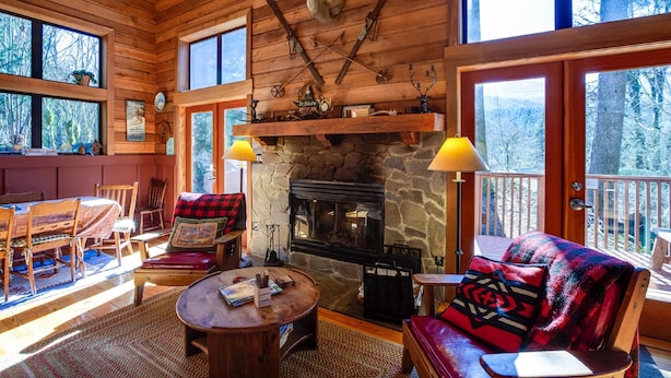 A cozy cabin interior with a stone fireplace, wooden furniture, and large windows offering a view of the forest. - Mt Baker Rim Cabin 44 - A Cozy Rustic Cabin With Modern Charm (Deming)