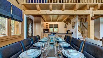 Un espace repas avec une longue table dressée pour six personnes, entourée de banquettes en cuir foncé.