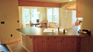 A kitchen with wooden cabinets, a central island with a sink, and a refrigerator. - Glacier Springs Cabin 2bedrooms, 2 Baths - hot tub & Pet Friendly! (Deming)