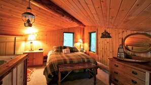A cozy wooden cabin bedroom with a bed, bedside lamps, a dresser, and a mirror. - Cabin #97 - 'pinecone' Log Cabin at the Lake That is Pet-friendly! (Deming)