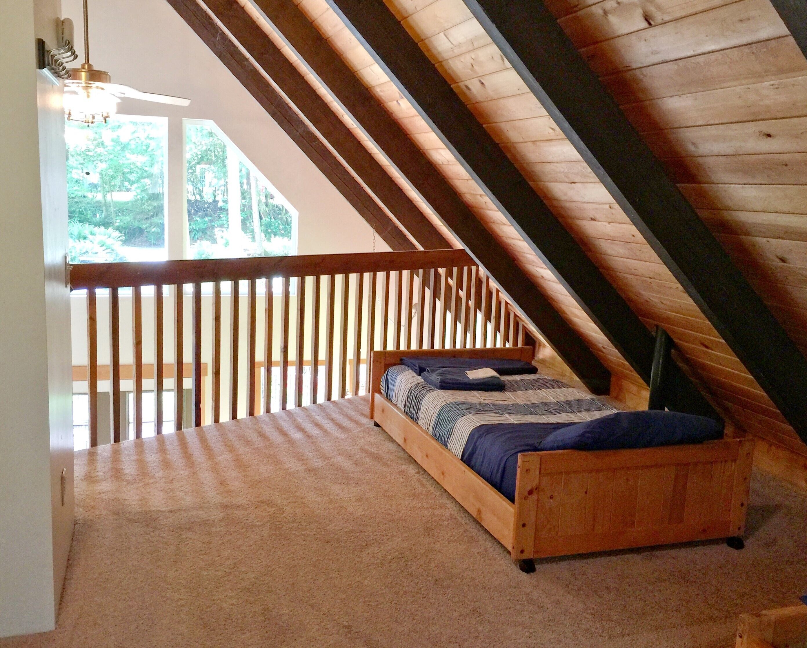Ein Schlafzimmer mit schrägen Wänden, einem hölzernen Bett und Blick ins Grüne.