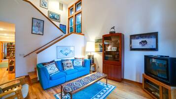 Una sala de estar con sofá azul, escalera de madera y televisor.
