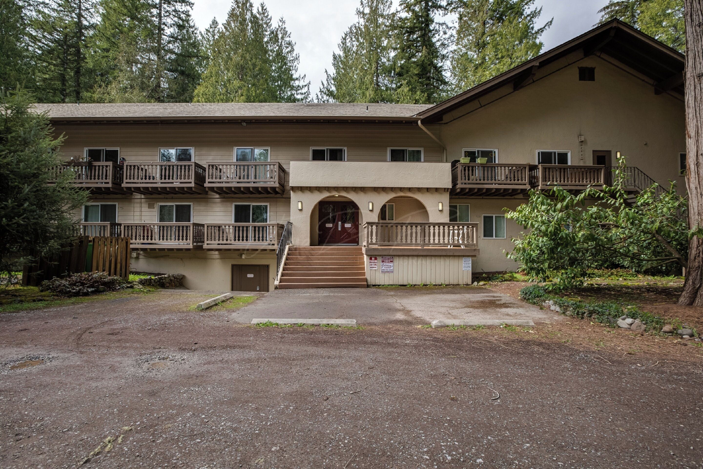 A multi-story building with balconies, a central entrance, and a surrounding natural landscape.