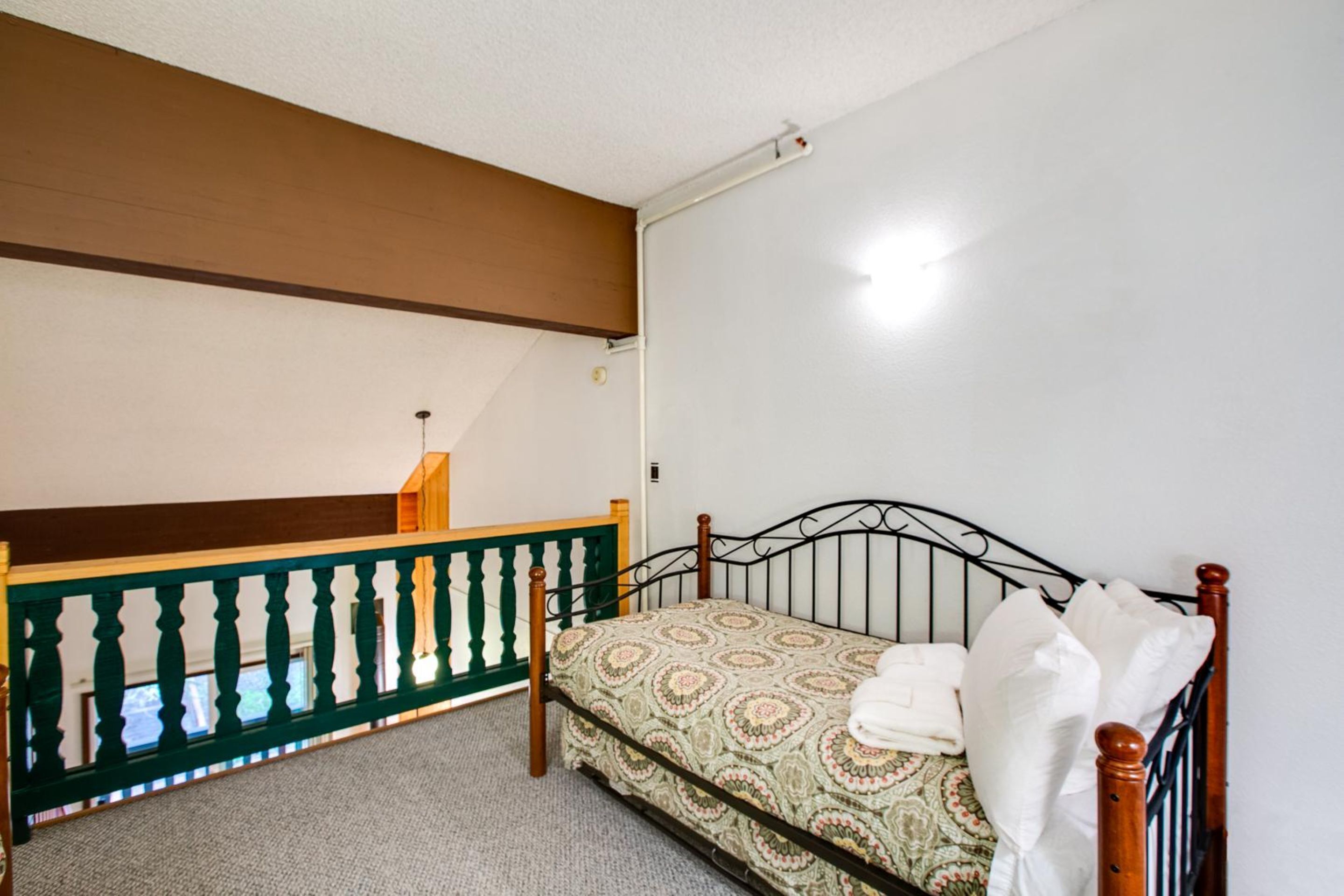 A bedroom with a single bed, a wooden headboard, a white wall, and a ceiling light.