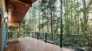A wooden deck with a green railing overlooking a forested area.