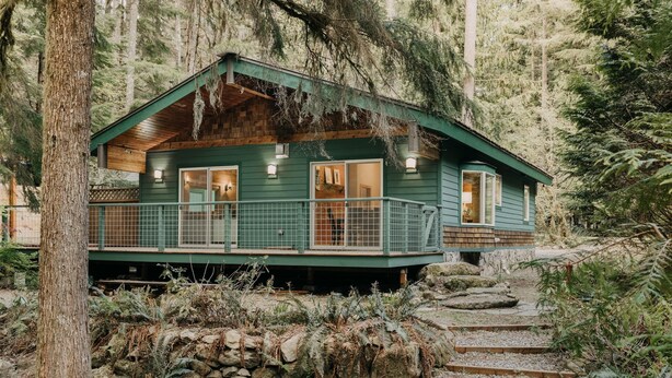 A cabin with a porch, surrounded by trees and rocks.