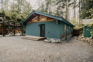 Une petite cabane à un seul étage, avec une façade verte, un porche à l’avant et une allée gravillonnée.