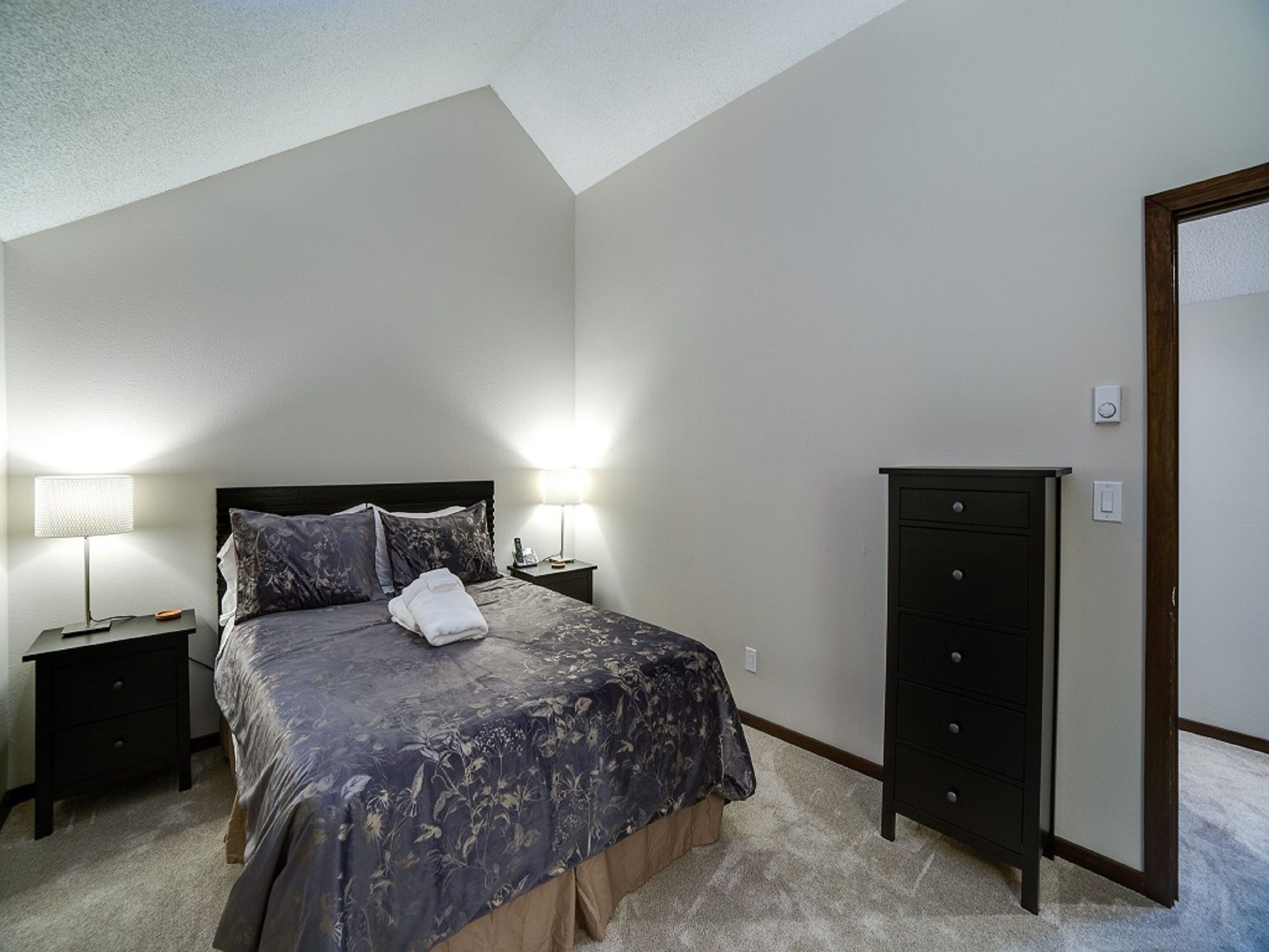 A bedroom with a bed, two bedside tables, a dresser, and a door.