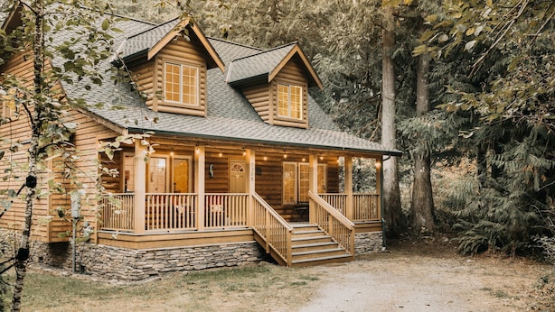 A log cabin with a porch, stone foundation, and a dirt path leading to the entrance.