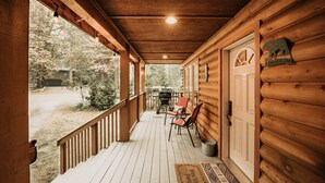 A wooden porch with a covered seating area, a door with a bear sign, and a view of the surrounding forest.