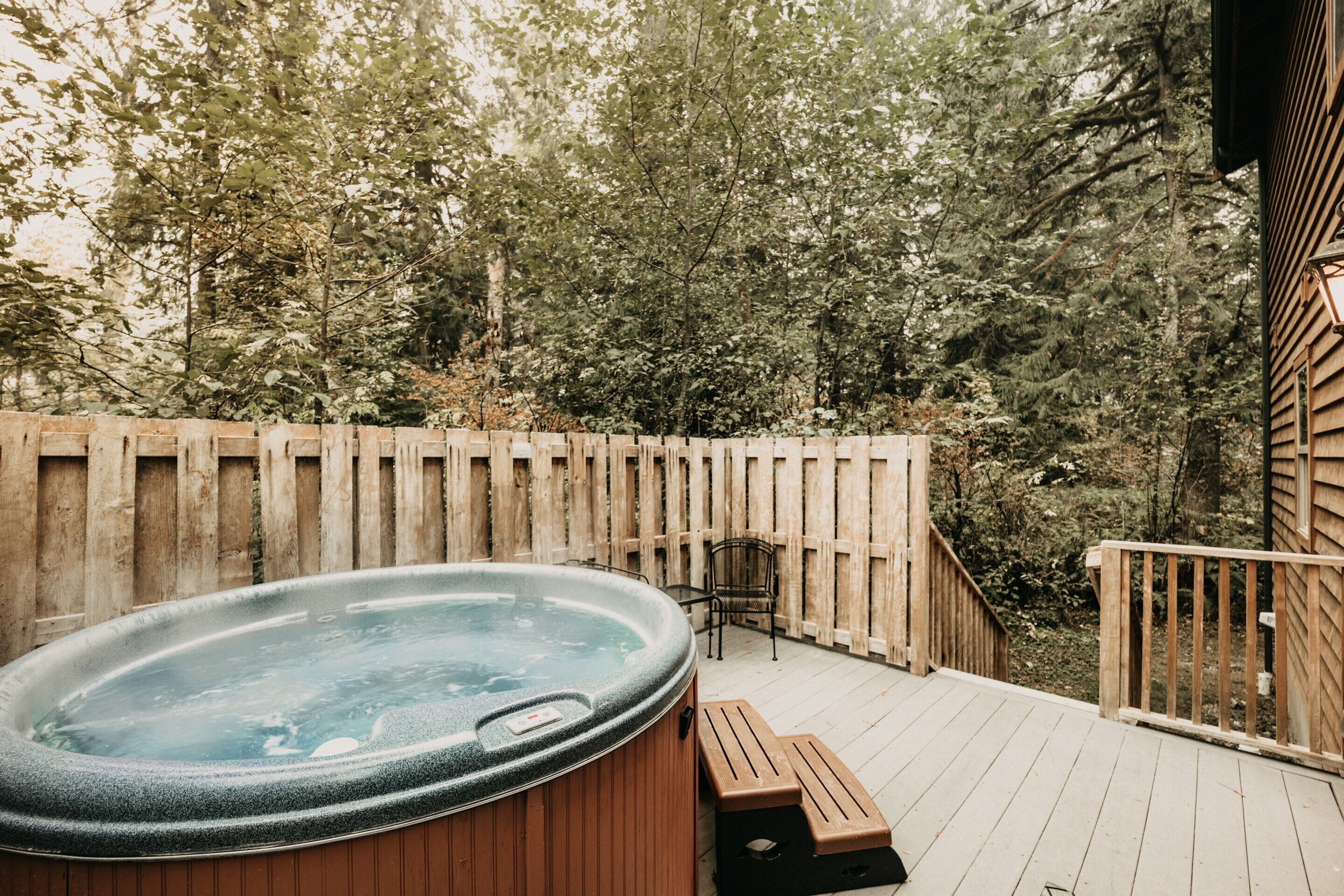 Un bain à remous sur une terrasse en bois, avec une clôture en bois et des arbres en arrière-plan.