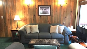 Ein gemütliches Wohnzimmer mit einem grünen Sofa, zwei Wandleuchten, einem gerahmten Bild und einem Fernseher auf einem Holzboden.