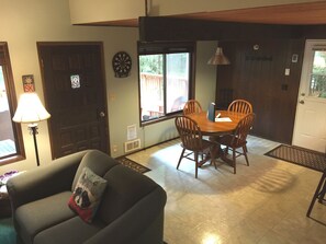 A dining area with a wooden table and chairs, a lamp, and a dartboard on the wall. - Snowline Cabin #98 A pet Friendly Cabin With a Wood Stove, hot tub and Wifi! (Deming)