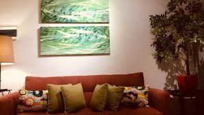 Ein Wohnzimmer mit einem roten Sofa, zwei abstrakten Bildern und einem Blumentopf.