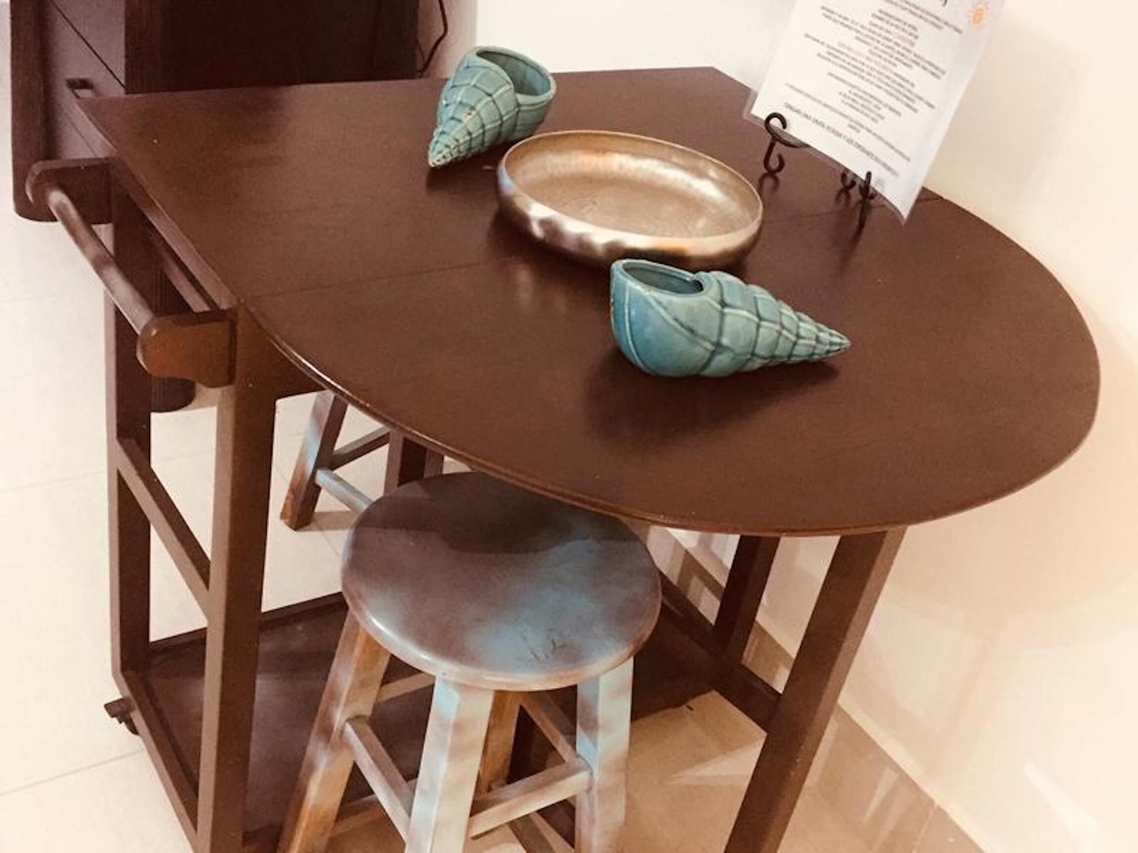 A small dining table with a brown tabletop, two teal-colored ceramic cups, a metal bowl, and a menu stand.