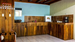 A kitchen with wooden cabinets, a refrigerator, a coffee maker, and a window. - Room-arenal Xilopalo Room (La Fortuna)