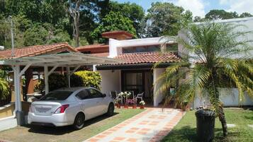 A residential property with a car parked in the driveway, a covered patio, and a small garden area with potted plants.