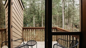 A wooden deck with two chairs and a table, overlooking a forested area. - Snowater Condo #57 - A Great 2-story Family Condo That Sleeps 6! (Deming)