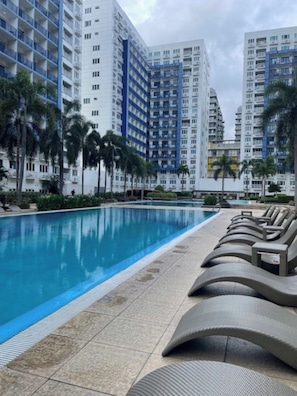 A swimming pool with lounge chairs, surrounded by tall residential buildings.