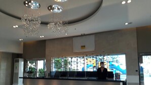 Moderni aula, jossa on vastaanottotiski, suuret kattokruunut ja suuret ikkunat, joista on näkymä.