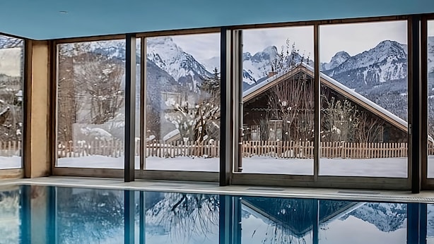 Une piscine avec vue sur des montagnes enneigées et un chalet en bois.