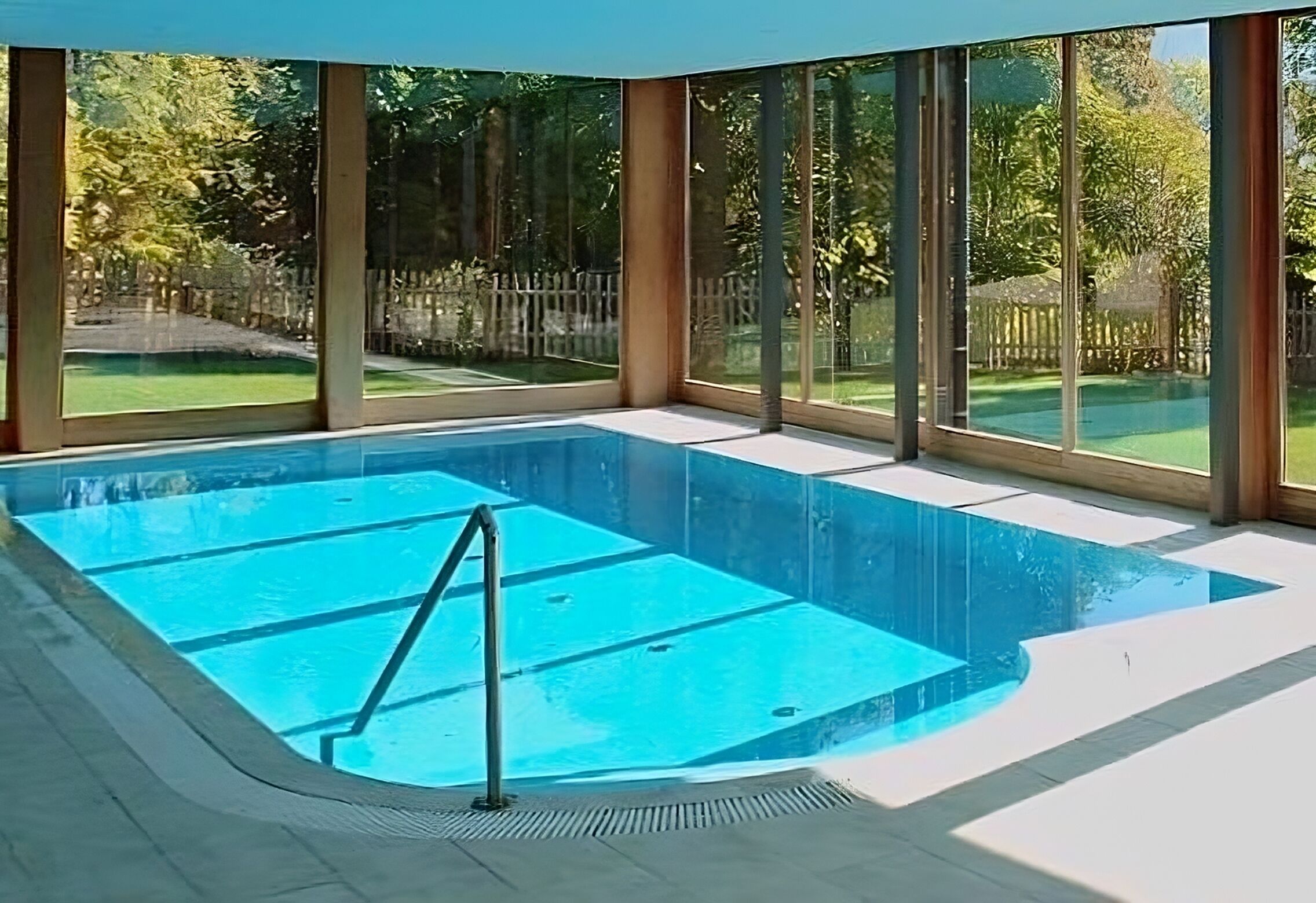 Une piscine intérieure avec des parois en verre transparent, un sol carrelé et un escalier en métal.