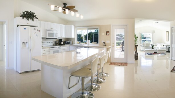 Cozinha moderna com armários brancos, uma ilha grande com banquetas, um ventilador de teto e vista para o exterior.