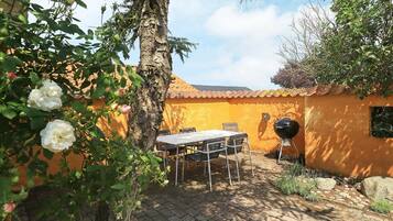 Une terrasse extérieure avec une table et des chaises, un barbecue et un arbre en fleurs.