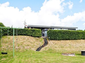 A modern house with a staircase leading to the entrance, surrounded by well-maintained hedges and a grassy area.