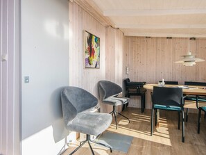 A modern dining area with wooden walls, a colorful abstract painting, and a mix of grey and black upholstered chairs.