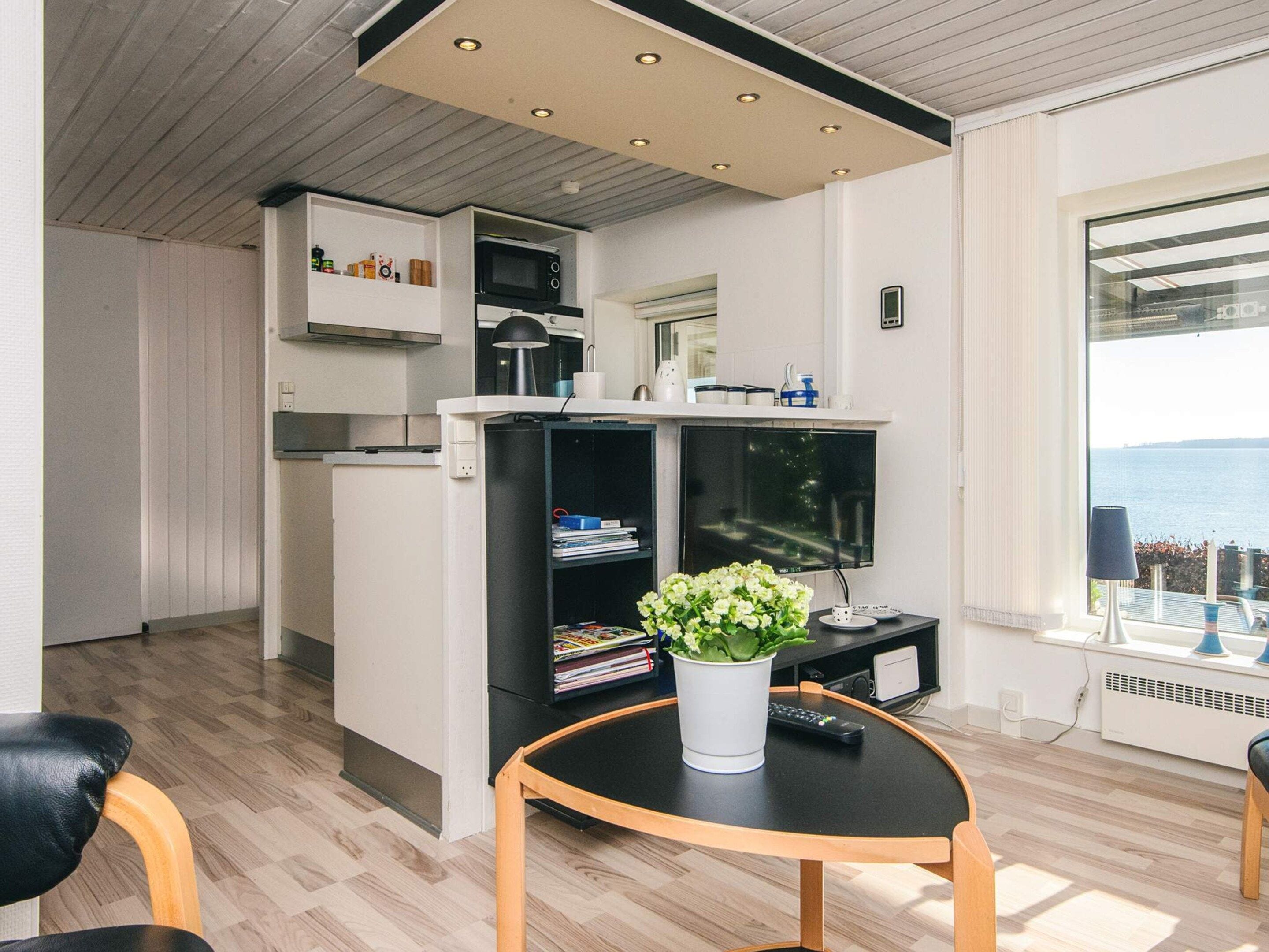 A compact living space with a kitchenette, a dining area with a round table, and a large window offering a view of the sea.