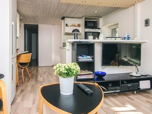 A modern kitchen with a microwave, oven, and built-in TV. There is a dining area with a chair and a table, and a small plant on the table.
