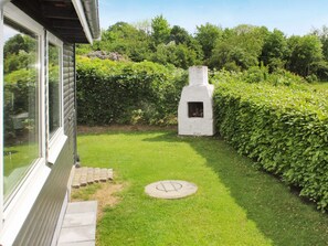 A well-maintained garden with a white outdoor fireplace, a paved pathway, and a hedge. - 4 Star Holiday Home in Juelsminde (Horsens)