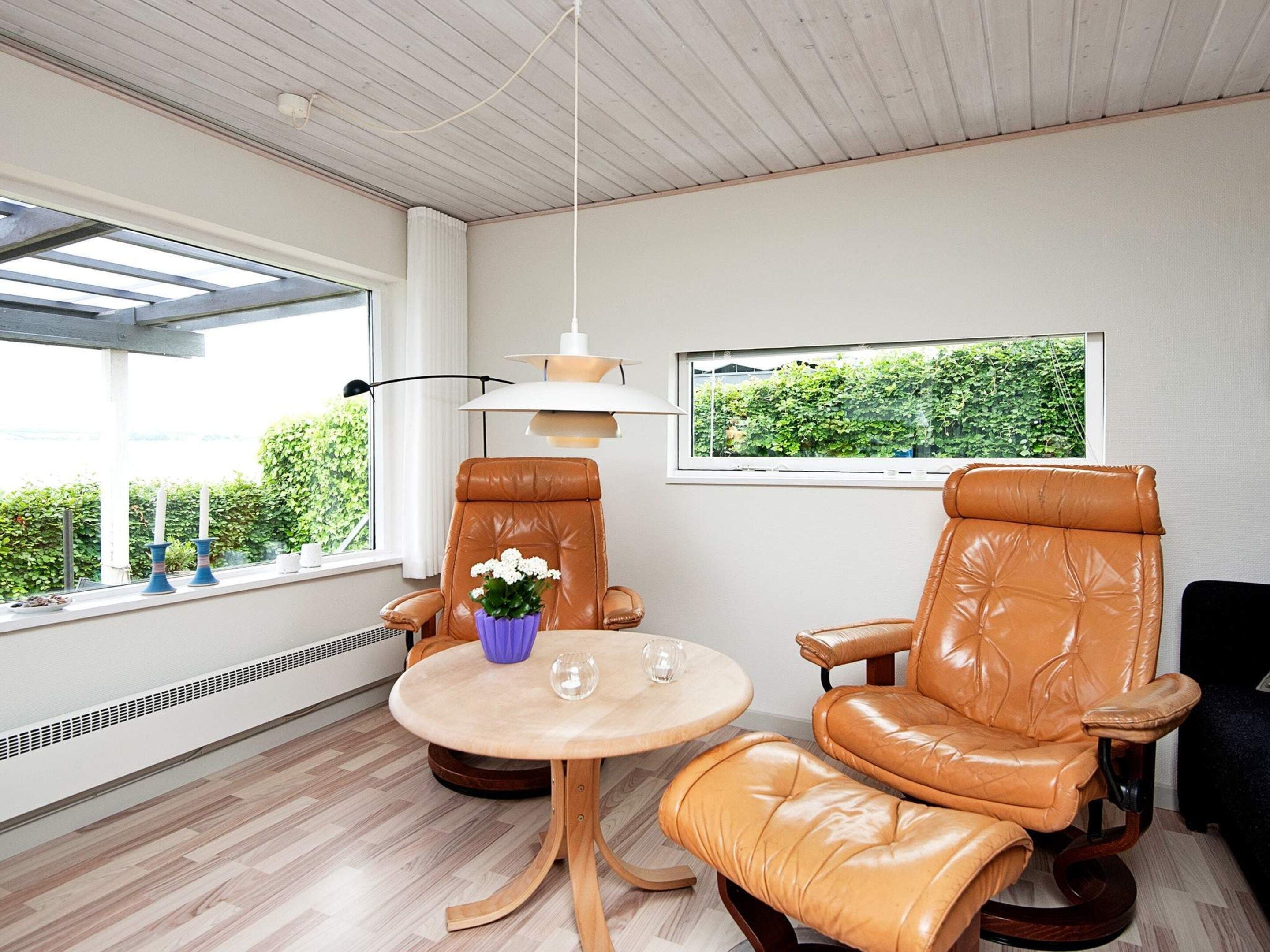 A room with two leather chairs, a small round table, a hanging lamp, and a window with a view of greenery.