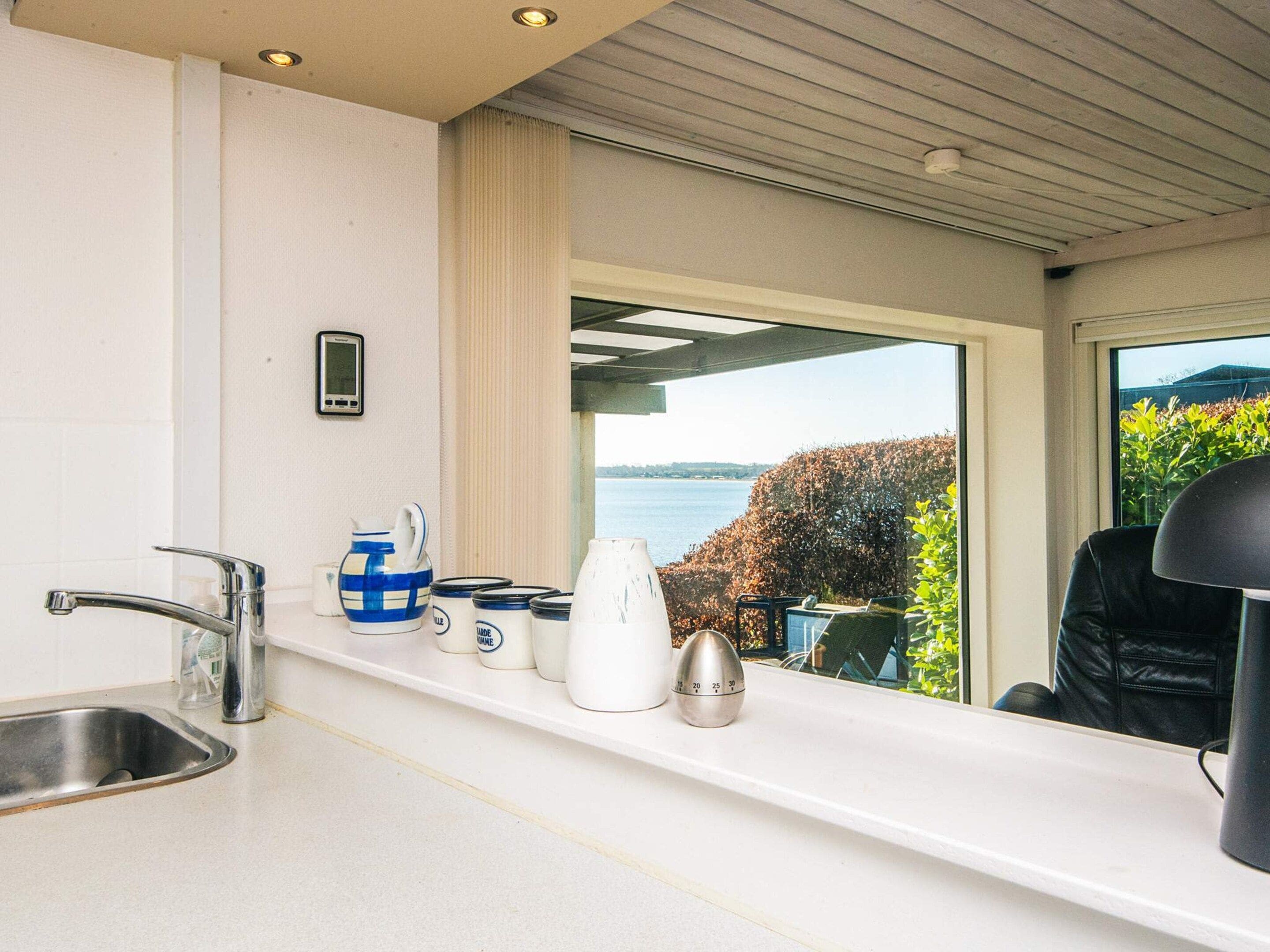 Una cocina moderna con un lavamanos de acero inoxidable, una encimera blanca y vistas al mar a través de amplios ventanales.