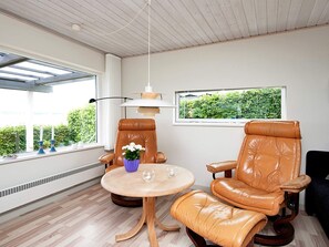A room with two leather chairs, a small round table, a hanging lamp, and a window with a view of greenery.