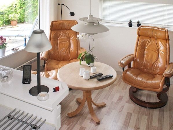 A modern living room with two leather armchairs, a round wooden table, a floor lamp, and a window with blinds.