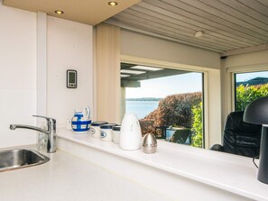 Et moderne køkken med en stålvask, en hvid bordplade og havudsigt gennem store vinduer.