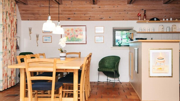 Un coin repas avec une table et des chaises en bois, une chaise verte, un petit îlot avec un évier et une fenêtre donnant sur un paysage verdoyant.