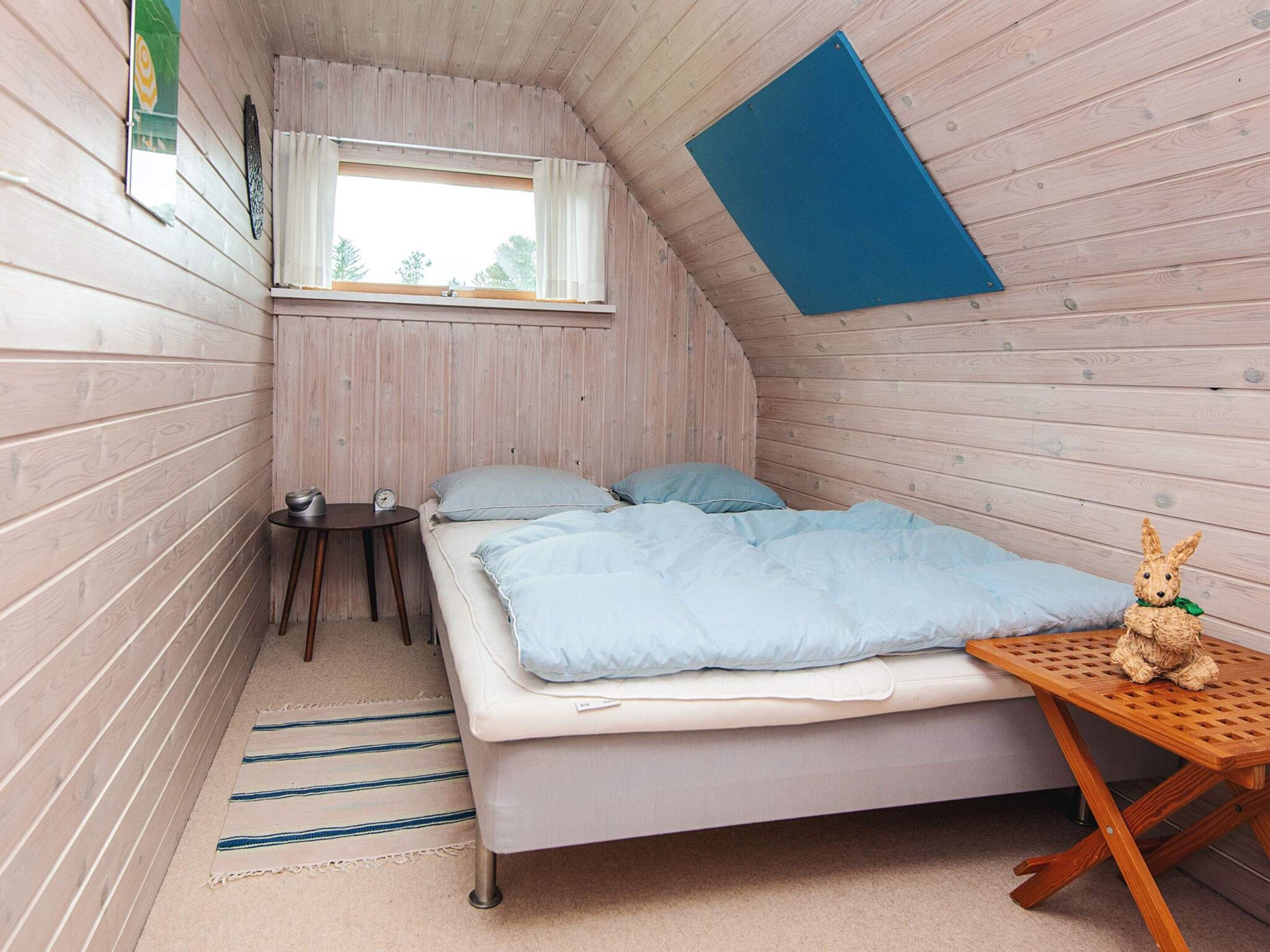 Ein kleiner, gemütlicher Raum mit schrägen Wänden, einem Bett mit Kissen, einem kleinen Tisch und einer dekorativen Hasenfigur.