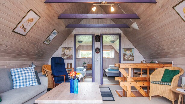 Una habitación acogedora estilo buhardilla con sofá, sillón, mesa y una silla de mimbre.