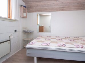 A bedroom with a bed, a small shelf, a mirror, and a window. - 8 Person Holiday Home in Glesborg (Glesborg)