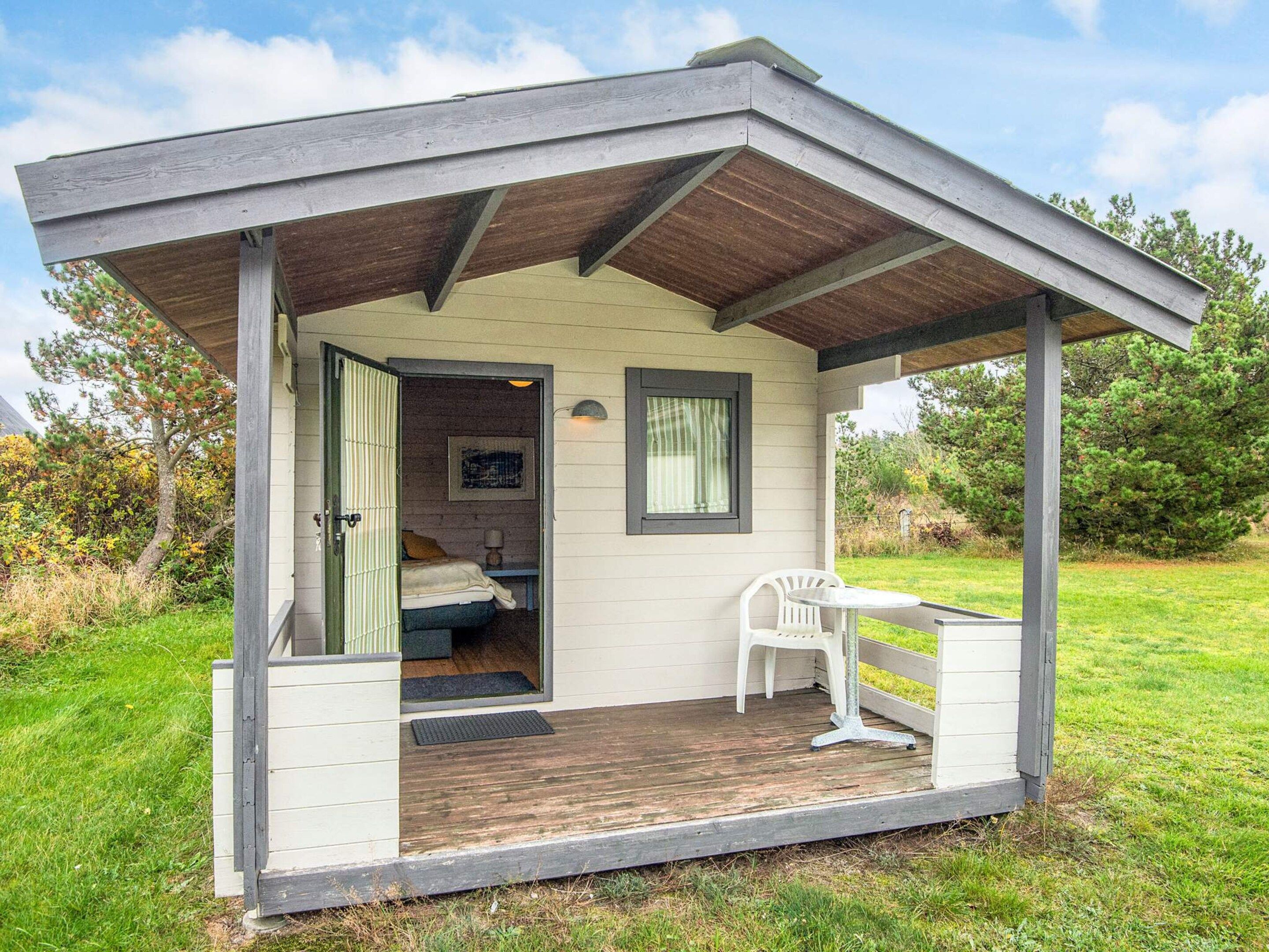Una cabaña pequeña de una sola habitación con una terraza de madera, una cama, una silla y un ventanal.