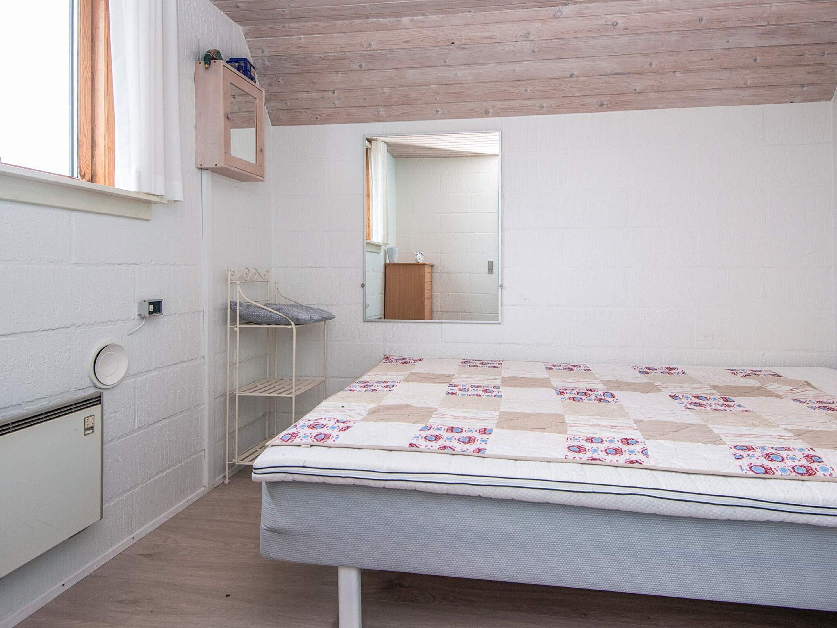 A bedroom with a bed, a small shelf, a mirror, and a window.